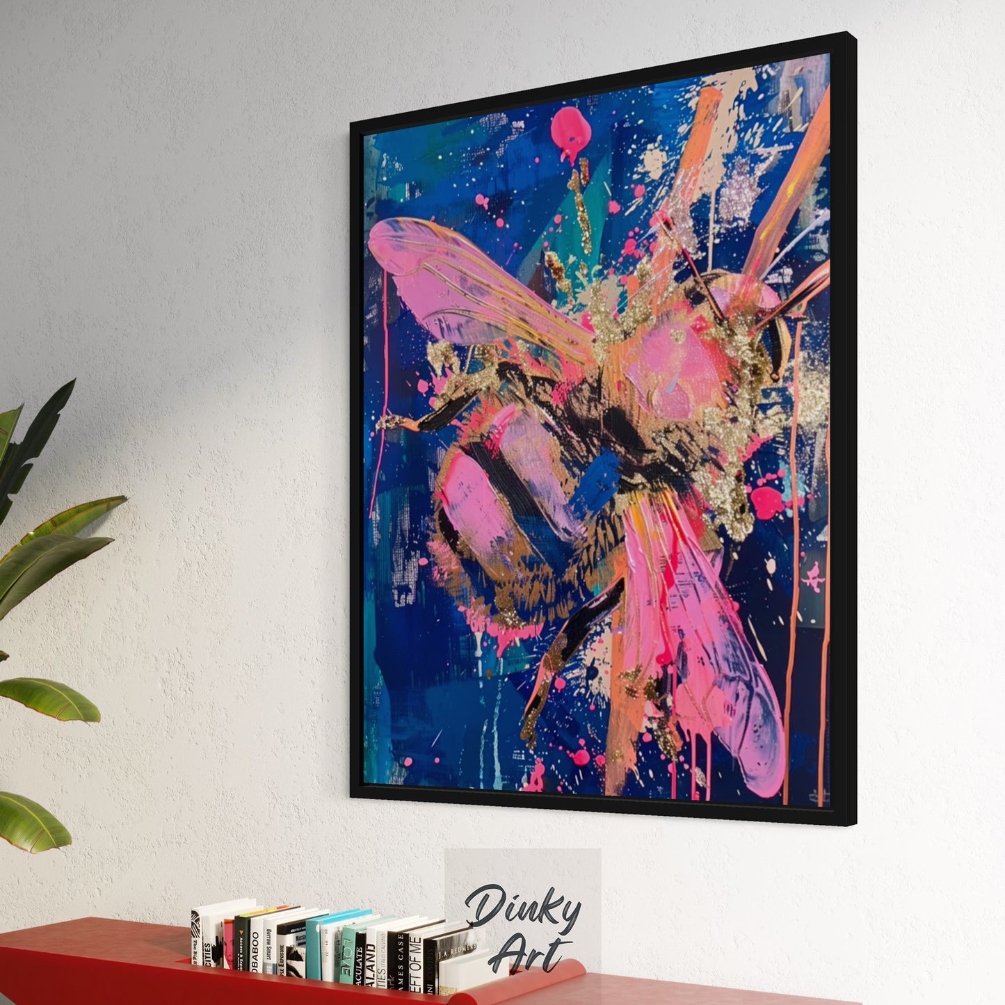 Framed abstract butterfly artwork on a wall with books and a plant below.