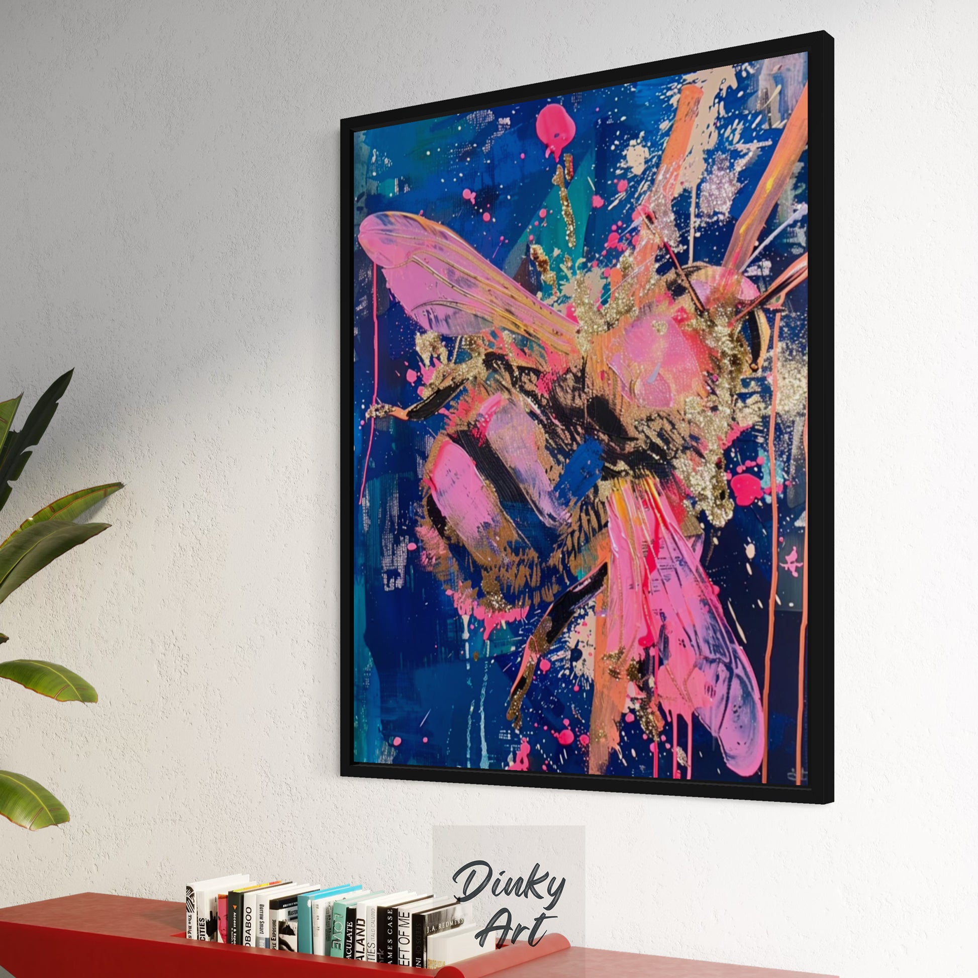 Framed abstract butterfly artwork on a wall with books and a plant below.